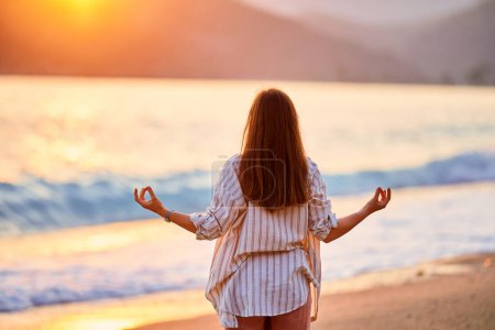 Photo for Back of calm serene peaceful woman in a lotus position meditates and enjoys a beautiful moment life on the seashore at sunset time - Royalty Free Image