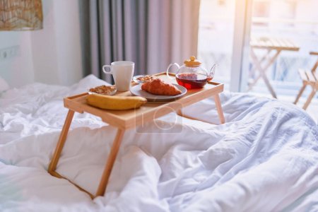 Tray with tasty breakfast in bed at light room in comfortable cozy morning