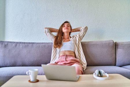 Téléchargez les photos : Jeune fille moderne occupée intelligente se détendre sur le canapé après une longue télécommande de travail en ligne à l'ordinateur - en image libre de droit