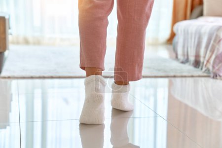 Téléchargez les photos : Jambes féminines en confortables chaussettes tricotées douces sur un plancher chauffant dans le salon à la maison - en image libre de droit