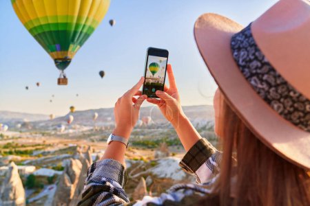 Photo for Girl tourist vacations in beautiful destination in Goreme, Turkey. Taking photo of flying air balloons in fabulous Kapadokya at sunrise, Anatolia - Royalty Free Image