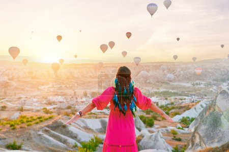 Photo for Alone spiritual free boho woman traveler makes wish in scenic valley in Anatolia, Kapadokya. Enjoying of flying hot air balloons at beautiful destination in Nevsehir, Goreme - Royalty Free Image