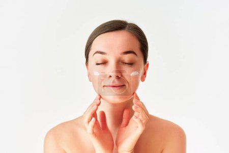 Foto de Retrato de mujer joven con crema facial para una hermosa piel sana sobre fondo blanco - Imagen libre de derechos