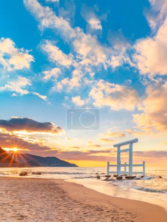 Photo for Sunset behind the coast of the Itoshima Beach in Fukuoka whith the white Shinto torii gate of Sakurai Futamigaura's Meoto Iwa Couple Rocks is standing in the sea. - Royalty Free Image
