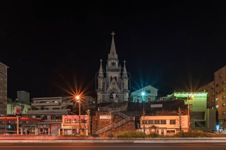 Foto de Sasebo, kyushu - dec 08 2022: Night front view of the lighted up Miura Catholic Church builded in gothic architecture on a hill overlooking the Japan National Route 35 of Sasebo city. - Imagen libre de derechos