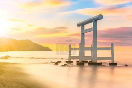 Sunset long exposure photography of a Japanese white wooden torii arch with its pillars in the sea along the Itoshima Beach of Fukuoka famous for Couple Rocks called Sakurai Futamigaura's Meoto Iwa.