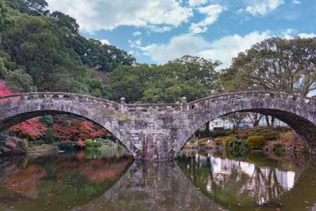 Téléchargez les photos : Nagasaki, kyushu - December 10, 2022: The Meganebashi or Spectacles Stone Bridge reflecting its symmetrical shape in the pond at Isahaya Park along the Honmyo River in Isahaya City. - en image libre de droit