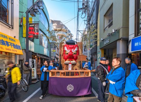 Téléchargez les photos : Tokyo, setagaya - january 28 2023: Japanese men dressed in happi kimono pushing a parade float with a giant tengu face in the street of Shimokitazawa during the tengu parade festival. - en image libre de droit
