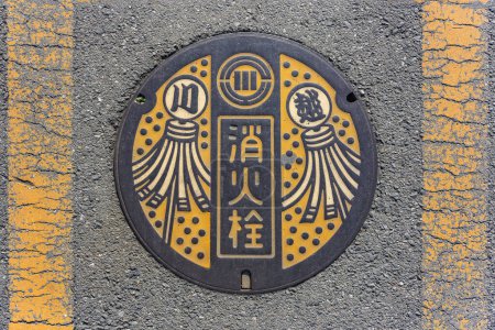 Foto de Tokyo, kawagoe - dic 31 2022: Suelo de asfalto con una tapa de alcantarilla de hierro fundido adornado con una ilustración que representa banderas matoi utilizadas en el período Edo por los bomberos japoneses para notificar a la gente de un incendio. - Imagen libre de derechos