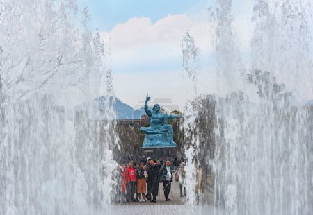 Téléchargez les photos : Nagasaki, kyushu - dec 11 2022 : jets d'eau d'une fontaine encadrant un touriste chinois à la statue de la Paix créée par le sculpteur japonais Seibo Kitamura inspiré par l'athlète Hiroichi Yoshida. - en image libre de droit