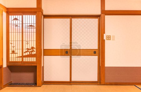 Téléchargez les photos : Mur d'une chambre typiquement japonaise avec tapis de tatami recouvrant le sol, portes fusuma et fenêtre shoji en papier de riz avec des décorations en bois évoquant un paysage du mont Fuji. - en image libre de droit