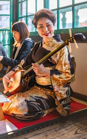 Photo for Nagasaki, kyushu - dec 14 2022: Shamisen instrument demonstration with tourists by a Japanese woman in kimono sitting in a traditional seiza pose in the First Ship Captain Quarters of Dejima island. - Royalty Free Image