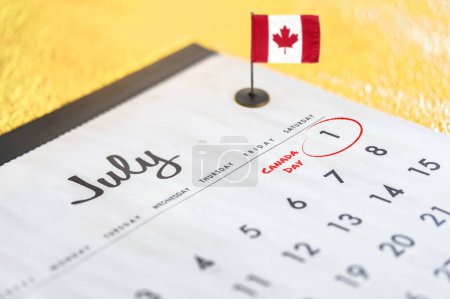 Téléchargez les photos : Photo en gros plan d'un calendrier consacré au mois de juillet et particulièrement à la date du 1er juillet entouré d'un marqueur rouge pour célébrer la fête nationale du Canada avec un mini drapeau de bureau sur l'arrière-plan - en image libre de droit