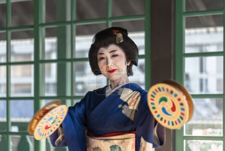 Foto de Nagasaki, kyushu - dic 14 2022: Mujer japonesa en kimono sosteniendo panderetas furidutsumi adornadas con diseños de tomoe durante una demostración de baile en el Barrio de los Primeros Capitanes de Barcos de la isla Dejima. - Imagen libre de derechos