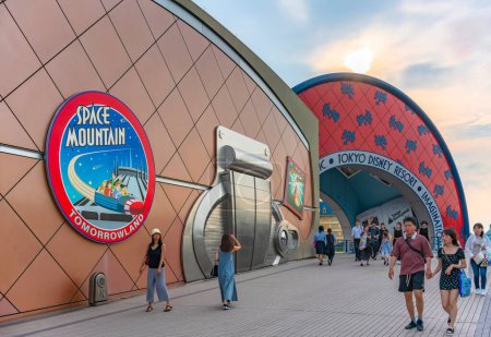 Photo for Chiba, japan - july 18 2023: People crossing walkway to Tokyo Disney Resort along the walls of Bon Voyage shop decorated with Space Mountain and Indiana Jones Adventure advertising posters at sunset. - Royalty Free Image