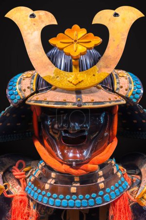 Photo for Tokyo, japan - june 27 2023: Japanese Kabuto helmet with a facial armor protecting the face adorned with a golden hanabishi crest part of a haramaki style armor laced with multi-colored threads. - Royalty Free Image