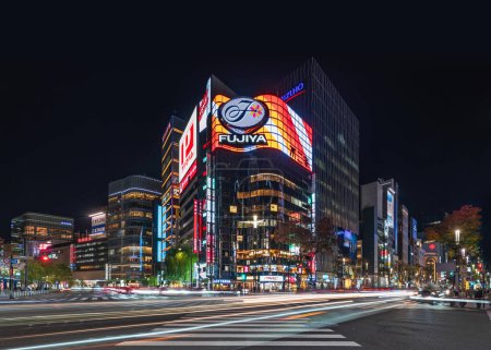 Foto de Tokyo, Japón - 29 nov 2021: Las calles Sotobori y Harumi se cruzan en Tokyo Downtown Ginza Scramble Crossing iluminado por la noche por el letrero de neón del edificio de restaurantes FUJIYA Sukiyabashi Store - Imagen libre de derechos