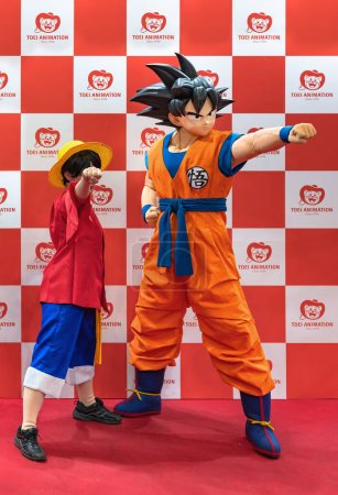 Téléchargez les photos : Chiba, japon - dec 18 2022 : Une jeune fille cosplayer portant le costume de personnage luffy d'une pièce balançant son poing vers l'avant avec une portée de Jump festa déguisée en Son Goku de Dragon Ball. - en image libre de droit