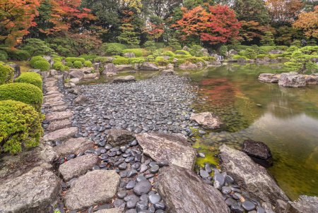 Foto de Fukuoka, kyushu - dic 07 2022: Paisaje natural otoñal que representa la orilla de guijarros mojada por la lluvia en el estanque del jardín tradicional japonés del jardín de Ohori con árboles momiji de arce que rodean. - Imagen libre de derechos