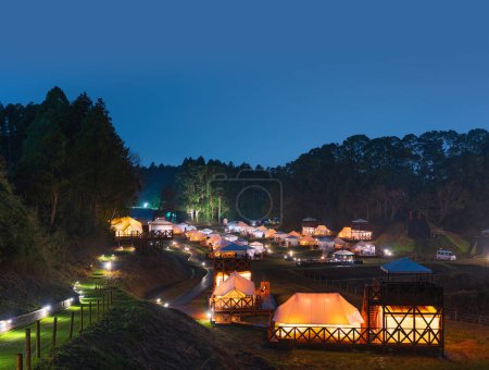 Téléchargez les photos : Japon, chiba - 25 mars 2023 : Paysage nocturne d'un chalet de ferme glamping avec un paysage de tentes et lofts glamour éclairés par des lanternes et des feux de bois dans la forêt de Nishitabe sous un ciel étoilé. - en image libre de droit