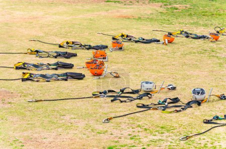 Photo for Orange colored half dome helmets arranged in a circle on yellowed lawn with Swift Quick Lock carabiners, handlebars and full body harnesses used for zip lining outdoor sports activities in a camping. - Royalty Free Image