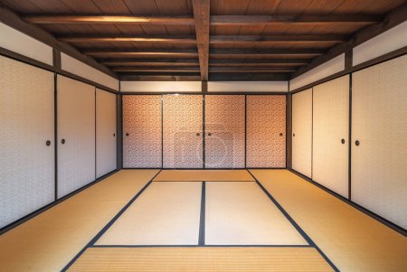 Téléchargez les photos : Intérieur d'une chambre typiquement japonaise spacieuse avec tapis de tatami couvrant le sol, portes fusuma et un plafond en bois avec poutres apparentes. - en image libre de droit