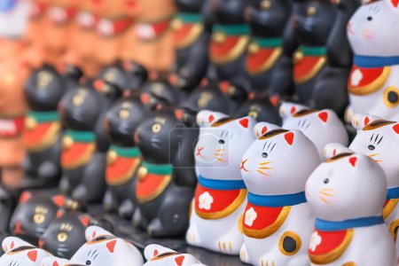 A bunch of aligned tiny and adorable stylized hand painted white Japanese manekineko cats lucky charm sculptures depicting to the famous beckoning cat and wearing bib adorned with a cherry blossom.