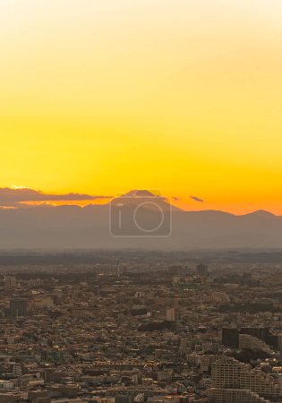Téléchargez les photos : Magnifique coucher de soleil à l'heure dorée surplombant un paysage urbain de la mégalopole de Tokyo dont les minuscules bâtiments à perte de vue contrastent avec le grand cône de la montagne Fuji à l'horizon - en image libre de droit