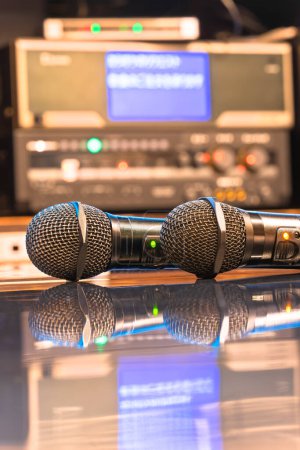 Téléchargez les photos : Deux microphones noirs dans une salle de karaoké japonaise réfléchissant sur une table avec une machine à karaoké et un contrôleur orné de boutons LED rétroéclairés pour régler le volume du microphone, l'écho et la mélodie. - en image libre de droit