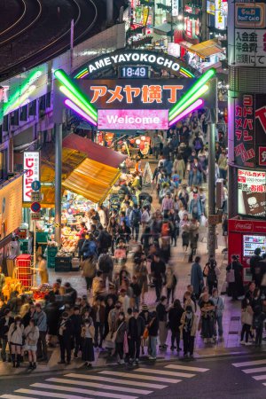 Foto de Ueno, Japón - 2 abr 2024: Multitud de turistas esperando por la noche al pie del iluminado arco de la calle del mercado de Ameya Yokocho con una pantalla escrita en inglés 'Welcome' sobre un fondo de flores de cerezo. - Imagen libre de derechos