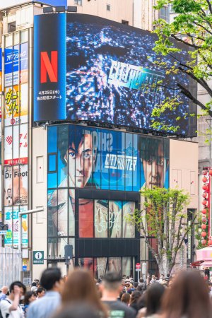 Photo for Tokyo, japan - apr 28 2024: Crowd walking towards the poster of the Netflix movie "City Hunter" or "Nicky Larson" under the movie trailer displayed on a curved screen at the exit of Shinjuku Station. - Royalty Free Image