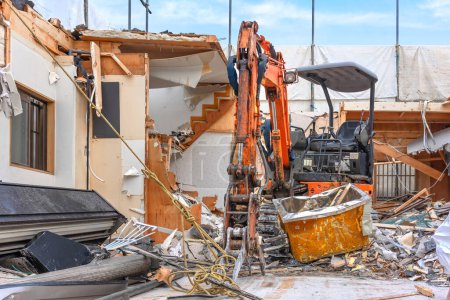 tokyo, japan - aug 28 2023: An orange backhoe loader equipped with a hydraulic excavator attachment to be able to grab heavy debris during the destruction of a traditional japanese wooden house.