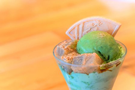 Ein traditionelles japanisches Dessert-Matcha-Eis-Parfait mit Würfeln von Agar-Gelee, bestreut mit geröstetem Sojabohnenmehl namens Kinako-Pulver und einer Higashi-Mochi-Waffel mit Kiefernmotiv.