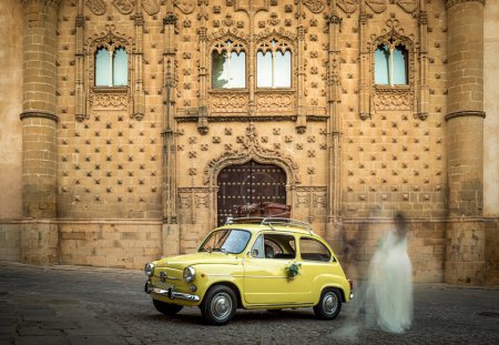 Photo for Old, small, yellow car to take the bride and groom to a wedding in a square in Baeza, a World Heritage City - Royalty Free Image