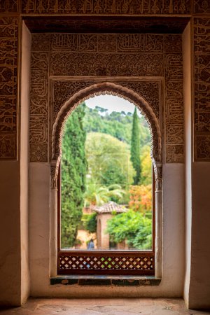 Fenster mit Reliefs der Nasridenpaläste der Alhambra in Granada, Spanien, mit den verschwommenen und farbenfrohen Gärten im Hintergrund