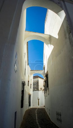 Foto de Pintura vertical de un estrecho callejón blanco del casco antiguo de Arcos de la Frontera, Cádiz, Andalucía, España, con arcos entre las casas y el cielo azul - Imagen libre de derechos