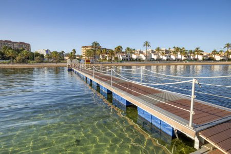 Foto de Puente de hierro y pasarela de madera sobre la playa cristalina de El Mar de Cristal, en el Mar Menor, Cartagena, España con el pueblo al fondo - Imagen libre de derechos