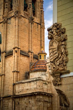 Foto de Foto vertical de la torre de la iglesia de Santa Justa y Sufina en Orihuela, Alicante, España con el noble escudo de armas de un edificio en primer plano - Imagen libre de derechos