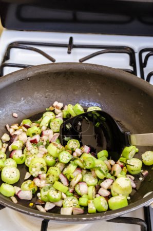 Téléchargez les photos : Faire frire une combinaison de gombo, radis et navet dans une poêle antiadhésive noire sur une cuisinière blanche et noire. - en image libre de droit