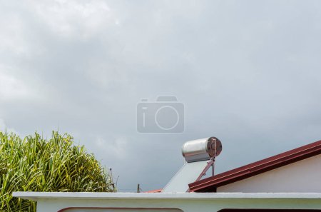 Foto de Es un cielo nublado sobre una casa con un solo tambor y un solo panel calentador de agua solar en su techo. - Imagen libre de derechos