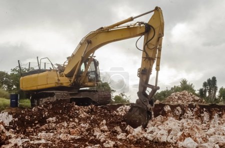 Photo for On a cloudy day a yellow excavator digs in the rocky ground. - Royalty Free Image