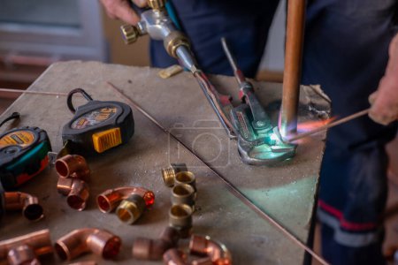 Photo for A worker welds copper pipes with a gas torch for central heating - Royalty Free Image