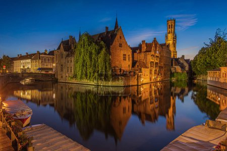 Rosenkranzkai am Abend in Brügge. Zentrum der alten Hansestadt mit Kanal zur blauen Stunde. Reflexe beleuchteter historischer Kaufmannshäuser und Glockentürme auf der Wasseroberfläche
