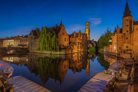 Zentrum der Altstadt von Brügge mit Blick auf den Rosenkranzkai. Alte belgische Hansestadt mit Kanal zur blauen Stunde. Reflexe beleuchteter historischer Kaufmannshäuser und Glockentürme auf der Wasseroberfläche