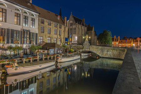 Photo for Illuminated houses on the canal in Bruges in the evening. Hanseatic city in Belgium at blue hour. Historic merchants' houses in the Hanseatic city. Reflections on the water surface - Royalty Free Image