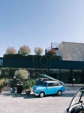 Photo for Surfboard on the roof of a vintage blue Trabant 601 car near a modern hotel. High quality photo - Royalty Free Image