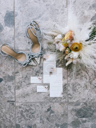 Photo for Wedding bouquet stands on a tile next to the bridal shoes, invitations and a ring. High quality photo - Royalty Free Image