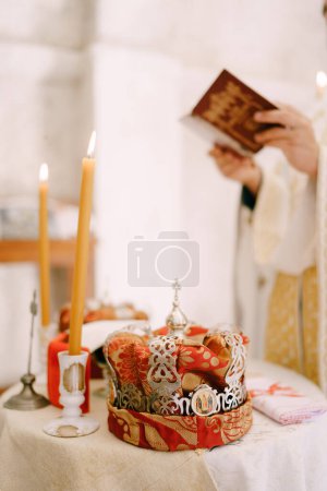 Téléchargez les photos : Le prêtre lit la Bible près de la table avec des bougies allumées et des couronnes de mariage. Découpé. Photo de haute qualité - en image libre de droit