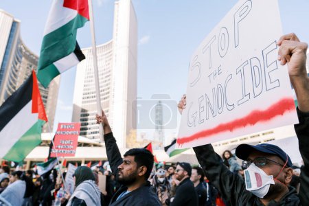 Foto de Manifestantes sostienen banderas palestinas y un letrero que dice PARAR EL GENOCIO en un entorno urbano con edificios altos en el fondo. Uno usa una máscara protectora. Foto de alta calidad - Imagen libre de derechos