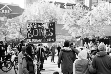 Foto de Escena urbana que representa una protesta. Una mujer sostiene un letrero que dice que Israel está construido por los huesos de los niños palestinos. Personas, árboles y edificios en el fondo. Foto de alta calidad - Imagen libre de derechos